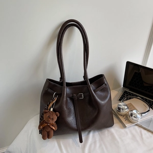 Detail of dark brown tote bag featuring smooth leather texture and a plush bear charm