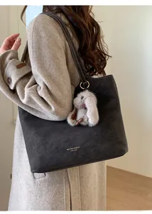 Detail of grey vintage leather tote bag with plush bunny charm and golden brand text