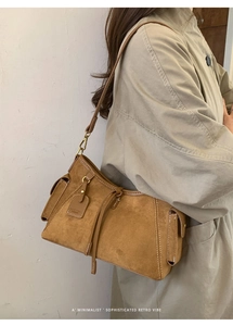 Detail einer braunen Wildleder-Schultertasche mit goldenen Schnallen und Fransen am Model