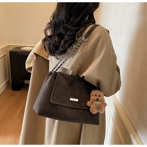 Makroaufnahme einer braunen Wildleder-Schultertasche mit Logo und Plüschbär-Anhänger