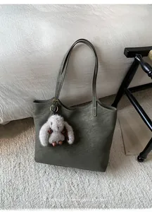 Detail of dark olive green leather tote bag with gold logo and plush rabbit pendant
