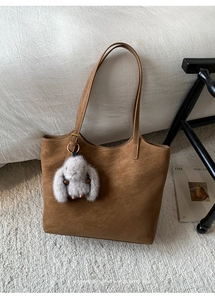 Detail view of brown tote bag textured leather with golden logo and plush rabbit charm