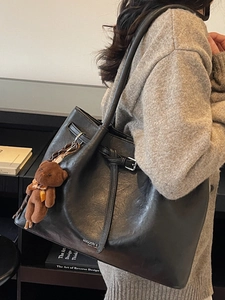 Minimalist black leather underarm tote bag with a decorative plush bear charm and strap buckle