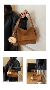 Close-up of brown suede shoulder bag with plush charm and embossed logo detail