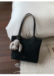 Detail of black tote bag with white stitching, gold hardware and plush bunny charm