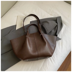 Detail of dark brown wing-shaped tote bag with matte PU leather and protective base studs