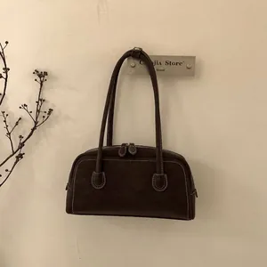 Close-up of dark brown suede shoulder bag with white contrast stitching and dual zippers