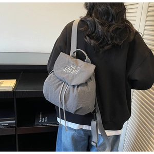 Detail view of gray drawstring backpack with bubble textured fabric and letter embroidery