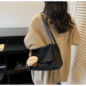Detail of minimalist black tote bag with plush charm on a beige sweater background