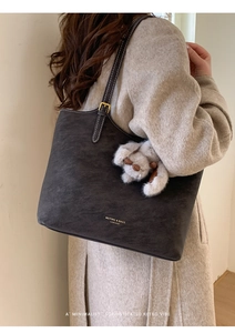 Detail of dark grey suede tote bag with plush dog charm worn over a beige wool coat