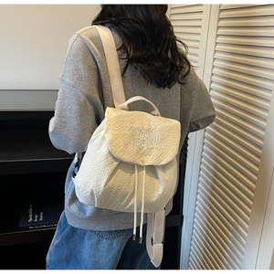 Close-up of cream textured fabric backpack featuring white YOU BEAR! embroidery and drawstring