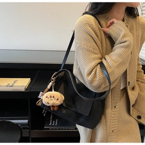 Detail view of black shoulder bag with chain strap and cute plush charm on a model