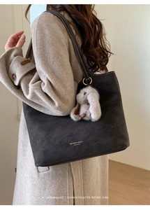 Detail of black suede tote bag with white contrast stitching and plush bunny pendant
