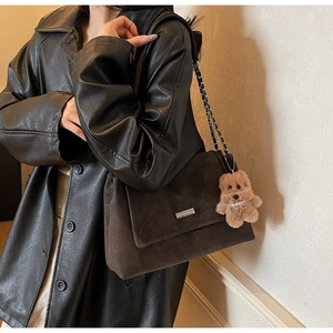 Detail einer dunkelbraunen Wildleder-Schultertasche mit Kettenriemen und Plüschbär-Anhänger