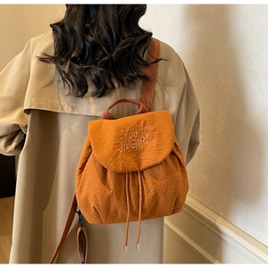 Detail of orange textured drawstring backpack featuring the YOU+ BEAR! embroidered flap