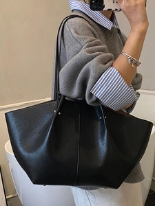 Minimalist black leather wing-shaped tote bag worn by a model in a casual setting