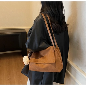 Detail view of brown suede shoulder bag with plush pendant and flap closure detail