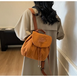 Detail of orange fabric backpack showing drawstring closure and letter embroidery