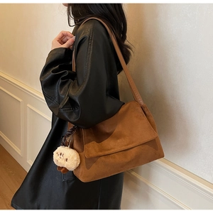 Close-up of brown suede shoulder bag with a cute plush bear charm on the side strap