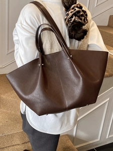 Deep brown retro oversized bat-shaped tote bag worn by a model in an indoor setting