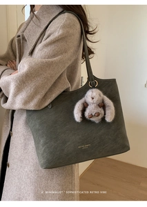 Detail of olive green vintage tote bag with gold logo and grey rabbit plush pendant