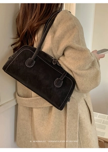 Detail view of black faux suede baguette bag with contrast white stitching on a model
