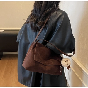 Detail of dark brown suede shoulder bag with plush charm and matte texture on model