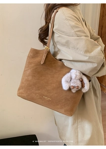 Close-up of vintage brown suede tote bag with golden lettering and plush rabbit charm