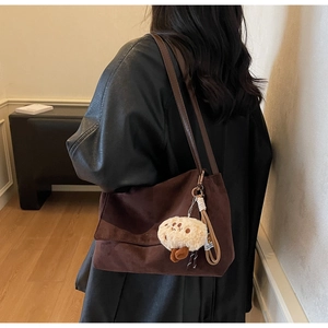 Close-up of brown suede shoulder bag with a cute plush bear charm in a home setting