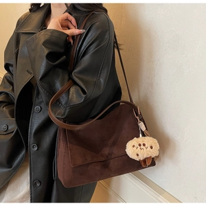Detail of suede shoulder bag with cookie charm accessory worn over a black coat