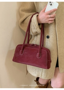 Detail of burgundy retro handbag with contrast stitching held by a model in a coat