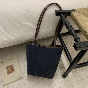 Detail view of large navy suede bucket bag with brown leather trim in a cozy home setting