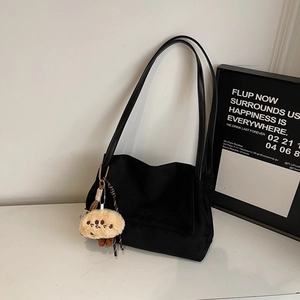 Detail of black suede tote bag with a cute plush charm accessory on white marble