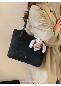 Detail of black leather tote bag with a cute plush bunny pendant and gold brand logo
