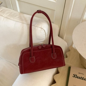 Detail of burgundy faux suede shoulder bag with white contrast stitching on sofa