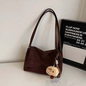 Detail view of brown suede shoulder bag with a cute plush mushroom pendant on white marble