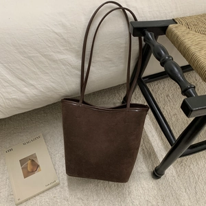Detail view of deep brown suede bucket bag with long shoulder strap in a cozy setting