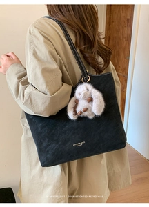 Detail of black suede tote bag with white stitching and plush rabbit charm on beige coat