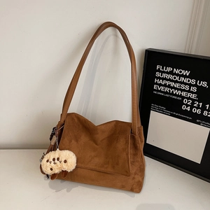Detailed texture of dark brown suede shoulder bag with a cute beige plush lamb pendant