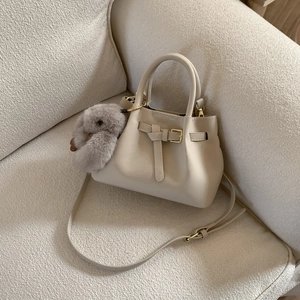 Close-up of beige leather tote bag with plush bunny charm on a cozy cream-colored sofa