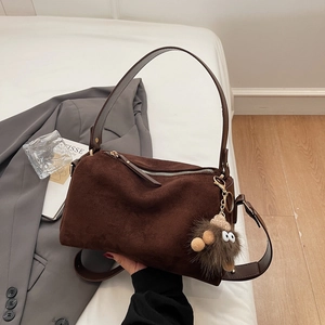 Detail einer braunen Wildlederimitat-Boston-Tasche mit Plüschanhänger und Metallteilen