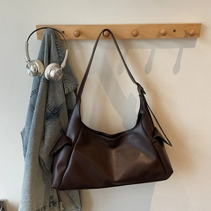 Détail d'un grand sac à bandoulière café foncé en similicuir sur un cintre en bois