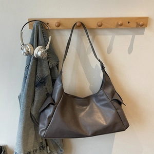 Détail d'un grand sac hobo en cuir mat gris foncé avec poches latérales sur un crochet