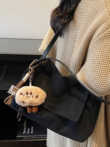 Minimalist black canvas shoulder bag with a cute plush paw pendant in a lifestyle view