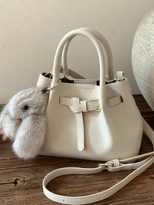 Creamy leather tote bag with a golden buckle and plush bunny charm on a wooden surface