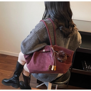 Detail view of burgundy suede tote bag with plush ball and beaded fringe on shoulder