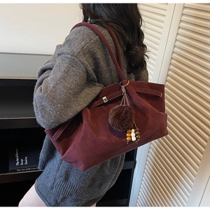 Macro shot of dark burgundy suede tote bag with decorative wooden beads and fur ball tassel