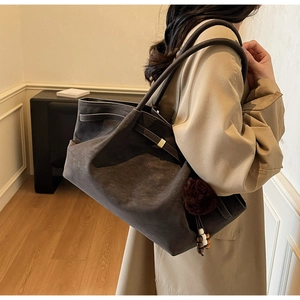 Detail of dark gray suede tote bag with brown pompom charm and thin shoulder strap