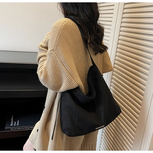 Detail of minimalist large black suede tote bag featuring a small metal logo plate