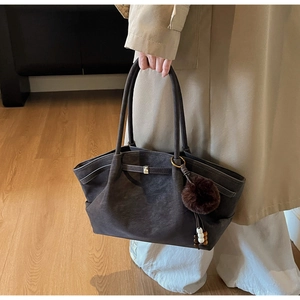 Detail of dark brown faux suede tote bag with metal buckles and decorative plush pendant